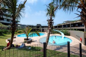 a swimming pool with people in a resort with palm trees at Pebble Beach 128 Umdloti Durban in Umdloti