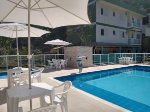 una piscina con sillas y una sombrilla junto a un edificio en Quitinetes Canto Verde Caraguá en Caraguatatuba