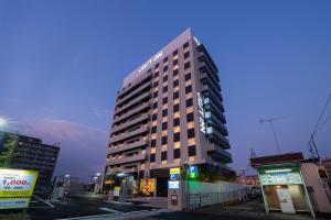松阪的住宿－Just Inn Matsusaka Station，一座高大的建筑,旁边有一个标志