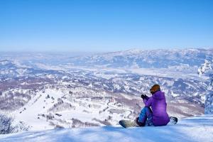 飯山市にあるホテルシルクイン斑尾の雪山の頂上に座るスノーボーダー