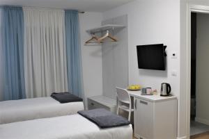 a hotel room with two beds and a desk and a tv at ZONA 30 Bike Guesthouse in Palmanova