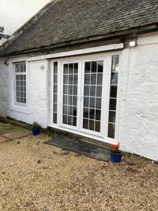 COACHMAN COTTAGE OUTSIDE HOT TUB في Beith: منزل أبيض مع باب زجاجي منزلق