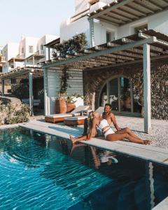a man and woman laying on the edge of a swimming pool at Belvedere Mykonos - Hilltop Rooms & Suites - The Leading Hotels of the World in Mýkonos City