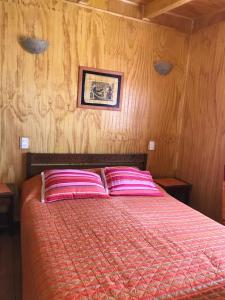 un letto con cuscini rosa in una camera da letto con pareti in legno di Mini Loft a El Quisco