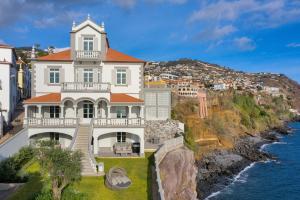 ein großes weißes Haus auf einer Klippe neben dem Wasser in der Unterkunft Luxury Barreirinha House old town by HR MADEIRA in Funchal