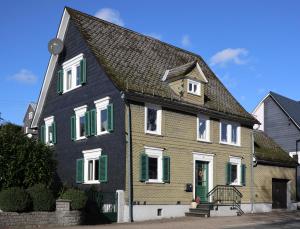 una casa negra y amarilla con persianas verdes en Ferienwohnung Weiß en Hilchenbach