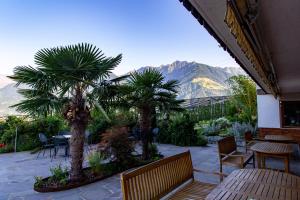 a patio with tables and chairs and palm trees and mountains at Pension Obertaberhof in Schenna