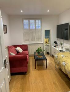 a living room with a red couch and a bed at Stylish Modern Studio, Mock Georgian House, Heart of Trendy Hackney & London in London