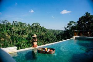 a woman in a hat standing next to a swimming pool at Suarapura Resort & Spa in Tegalalang