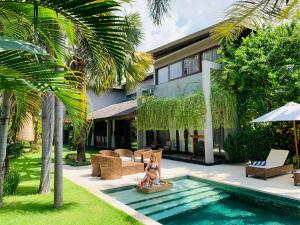 a woman sitting on a chair next to a swimming pool at Kamehameha Luxury Villa in Seminyak