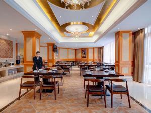 a man standing in a dining room with tables and chairs at Vienna Hotel(Shanghai Chongming Lvhai Road.) in Shanghai