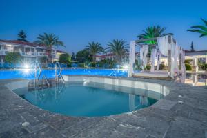 a pool at night with palm trees and buildings at Golden Sun Hotel in Kalamaki