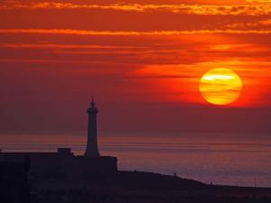 a sunset with a lighthouse in front of the ocean at Riad A La Belle Etoile in Sale