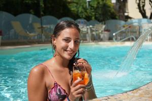 una mujer en una piscina sosteniendo una bebida en Hotel Pineta, en Bellaria-Igea Marina