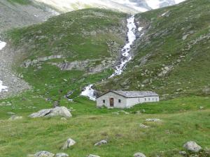 a small white building in a field with a waterfall at Oberschoellberghof in Lutago