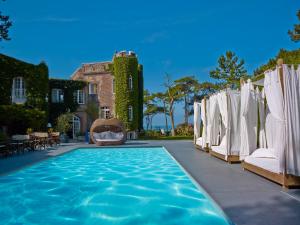 a pool with white umbrellas and chairs in front of a house at Domaine Saint Clair - Le Donjon in Étretat