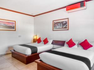 2 camas en una habitación de hotel con almohadas rojas en Monte Salerno Hotel & Suites, en Montemorelos