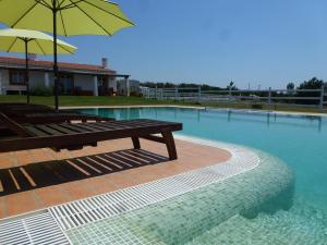 a swimming pool with a bench and an umbrella at SeteQuintas in Zambujeira do Mar