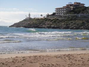 a beach with waves and a lighthouse in the background at Aparthotel El Faro in Cullera