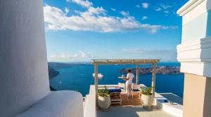 a man standing on a balcony with a view of the water at Iconic Santorini, a Boutique Cave Hotel in Imerovigli