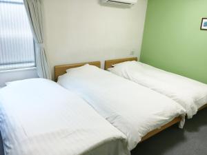 two beds in a room with white sheets and a window at Shin-Okubo City Hotel in Tokyo