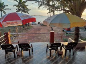 two umbrellas and chairs on a beach with the ocean at Leon Hide Out Guest House in Vasco Da Gama