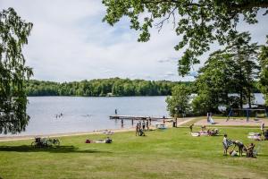 um grupo de pessoas na praia em um lago em Halens Camping och Stugby em Olofström