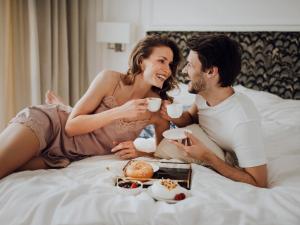 a man and a woman sitting on a bed with food at Empire Apart OVO in Wrocław