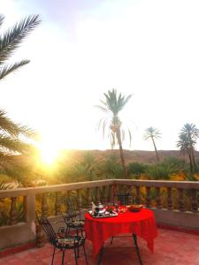 una mesa roja y sillas en un balcón con palmeras en Kasbah Elmehdaoui en Skoura