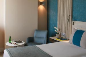 a hotel room with a bed and a blue chair at Occidental Faro in Faro