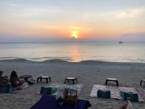 um grupo de pessoas sentadas na praia assistindo o pôr do sol em Moonwalk Lanta Resort em Ko Lanta
