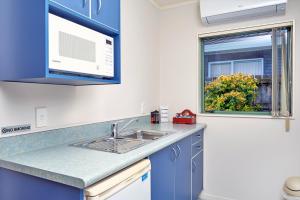 kuchnia z niebieskimi szafkami, umywalką i oknem w obiekcie Barringtons Motor Lodge w mieście Whakatane