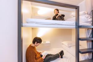 a man sitting on the floor in a room with bunk beds at &AND HOSTEL MINAMISENJU in Tokyo