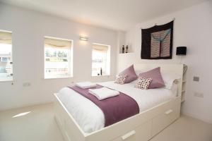 a white bedroom with a large bed with purple pillows at Veeve - Modern Edwardian in London