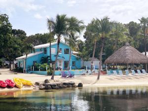 a beach with chairs and a blue house and palm trees at The Pelican Key Largo Cottages in Key Largo