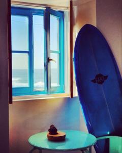 uma prancha de surf azul ao lado de uma mesa e de uma janela em Azenhas do Mar West Coast Design and Surf Villas em Sintra