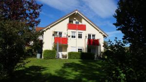 a white house with red trim on a green yard at BodenSEE Apartment Wasserburg "Im tiefen Brunnen" in Wasserburg am Bodensee