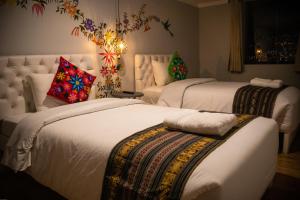 two beds in a bedroom with white sheets and colorful pillows at Home Garden Hotel in Cusco