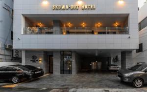 a building with two cars parked in a parking lot at Brown Dot Hotel Deokcheon in Busan