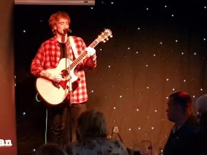 a man playing a guitar on a stage at 185 Belle Aire, Beach Road, Hemsby, Norfolk, NR29 4HZ in Hemsby