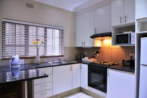 a kitchen with white cabinets and a sink and a microwave at Rivonia Premier Lodge in Johannesburg