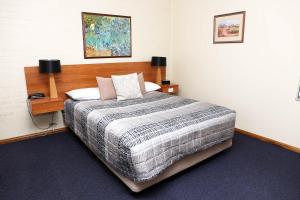 Schlafzimmer mit einem großen Bett mit einem Kopfteil aus Holz in der Unterkunft Westwood Motor Inn in Armidale