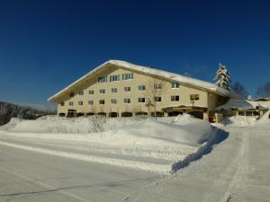 a building covered in snow next to a road at K's House Hokkaido - Asahidake Onsen Hostel in Higashikawa
