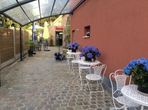 un patio con mesas blancas y sillas con flores púrpuras en Biotina, en Lebbeke