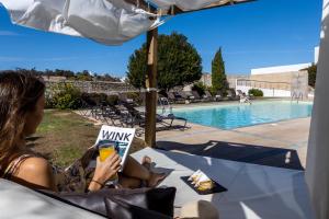 a woman sitting in a chair reading a book next to a pool at Pousada Convento de Tavira in Tavira