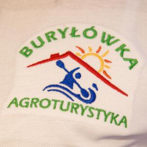 ein Logo auf einem weißen Hemd mit der Sonne und einer Person, die eine Welle reitet in der Unterkunft Agroturystyka Burylowka in Osiecznica