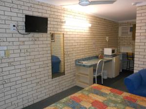 een kamer met een witte bakstenen muur, een bureau en een tv bij Cara Motel in Maryborough