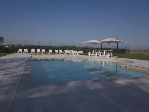 - une piscine avec des chaises blanches et un parasol dans l'établissement B&B La Corte Dei Vizi, à Clauiano