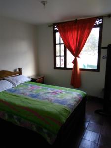 1 dormitorio con 1 cama con cortina roja y ventana en Posada De Los Santos Hotel Rural, La Candelaria, en Ráquira