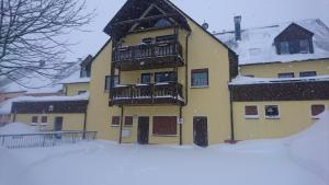 un bâtiment jaune avec un balcon dans la neige dans l'établissement Ferienwohnung Dachspitze mit Tiefgaragenstellplatz und Skiraum, à Kurort Oberwiesenthal